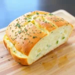 A loaf of savory garlic bread with a golden crust, sliced and topped with melted garlic butter and fresh parsley.